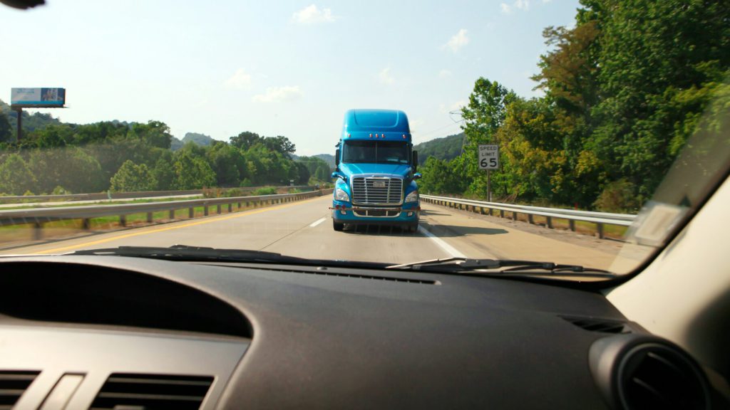 A tractor-trailer approaching on a highway, seen from inside a car